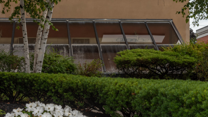 Exterior facade with groups signage, angled glass awning, pink and white flowering shrubs in dark mulch beds, birch trees