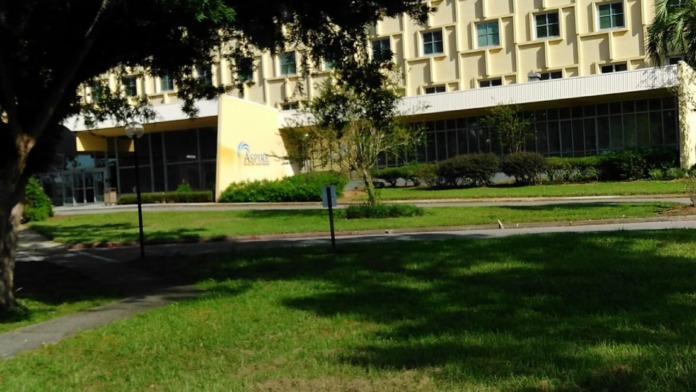Exterior view of multi-story Aspire Health Partners building with yellow facade, mature trees, and landscaped lawn area