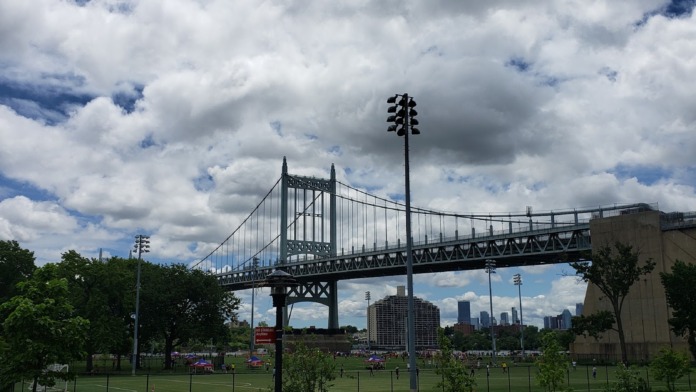 Outdoor grounds featuring sports field, directional signage, mature trees, and distant bridge structure