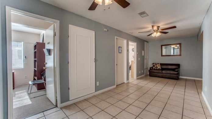 Interior hallway with multiple treatment room doors, seating area, natural light from windows, and neutral wall colors