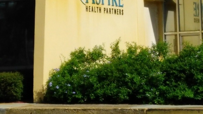 Exterior building wall showing Aspire Health Partners logo and branding on yellow facade with landscaping