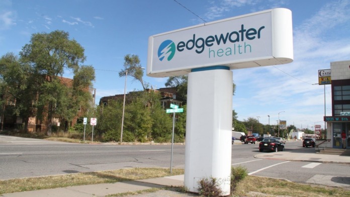 Exterior sign displaying Edgewater Health logo and branding along West 6th Avenue with street and surrounding buildings visible