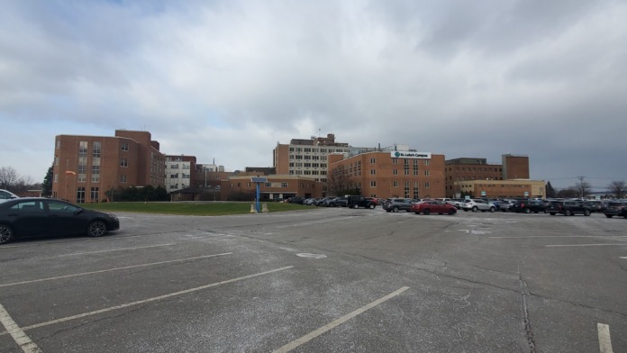 Exterior parking lot showing lined spaces, facility buildings with brick facade, landscaping, and clear sky