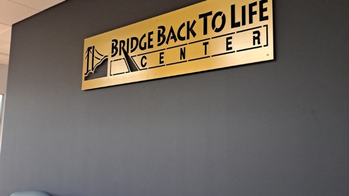 Interior waiting area showing facility's yellow Bridge Back to Life Center signage on dark gray wall with upholstered seating chairs below.