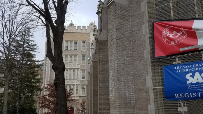 Exterior side view of stone building with decorative architectural details, concrete pathway, and adjacent structures