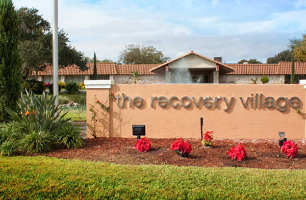Exterior view of facility signage with landscaped flower beds and buildings visible in background