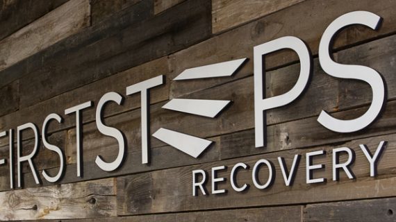 Exterior signage showing First Steps Recovery facility name on wooden architectural feature