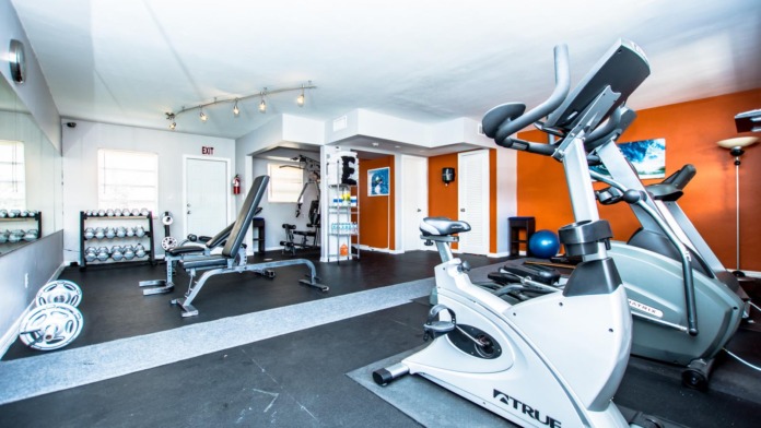 Interior fitness facility with stationary bikes, weight equipment, dumbbells, orange accent walls, and multiple exercise machines
