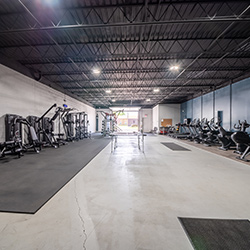 Interior fitness center with exercise equipment, mirrored walls, high industrial ceilings, and polished flooring