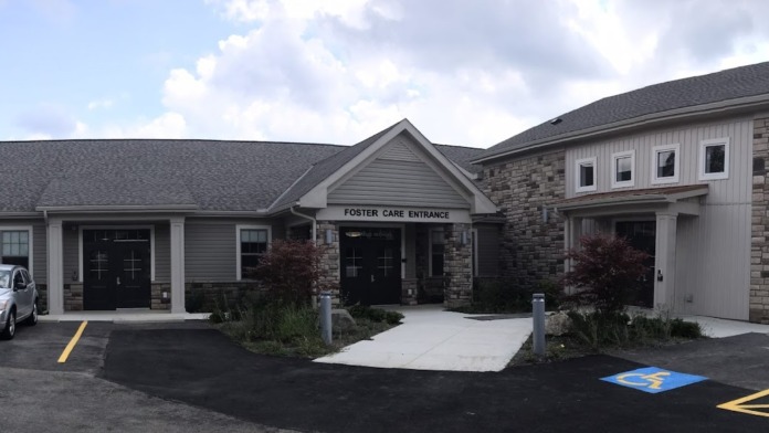 Exterior view showing Foster Care Entrance signage, stone and siding construction, accessible parking spaces, landscaping, and parked vehicle