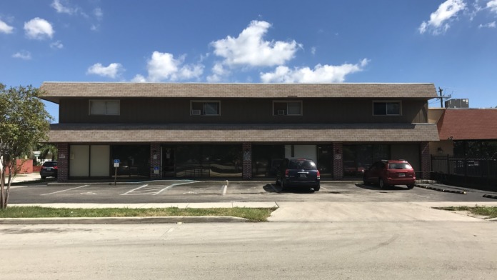 Exterior front of treatment center building with brick facade, large glass windows, entrance doors, traffic cones, and parking spaces.
