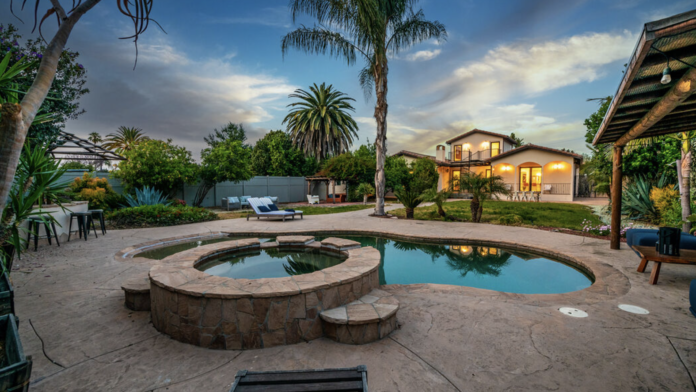Exterior courtyard with rectangular spa water features, lounge seating, mature palm trees, and Spanish colonial architecture at dusk