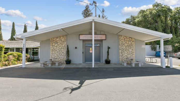Exterior front view showing facility entrance with stone facade, covered entry portico, landscaping, and parking area