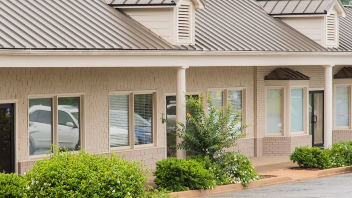 Exterior front entrance showing brick facade, metal roof, covered porch with landscaping and parking area visible