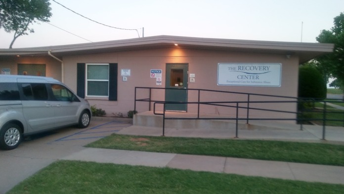 Exterior showing tan building front with metal accessibility ramp, railings, entrance doors, and parked vehicle visible.