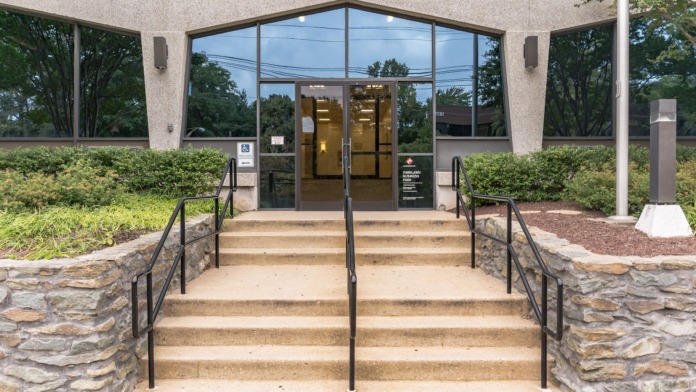 Exterior front entrance showing stairs, accessible ramps with handrails, glass doors, and mature landscaping