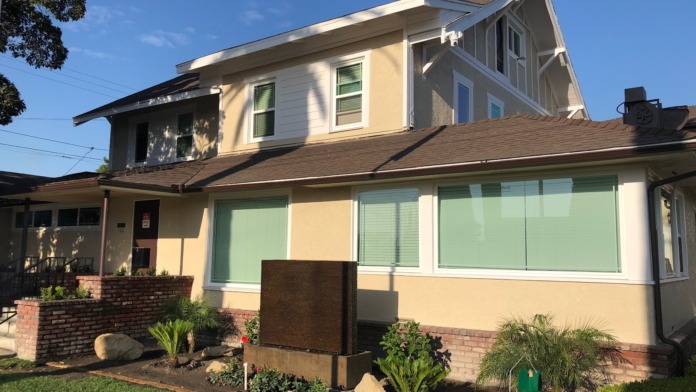 Exterior front facade of treatment facility with cream-colored siding, brick foundation, large windows, and landscaped grounds