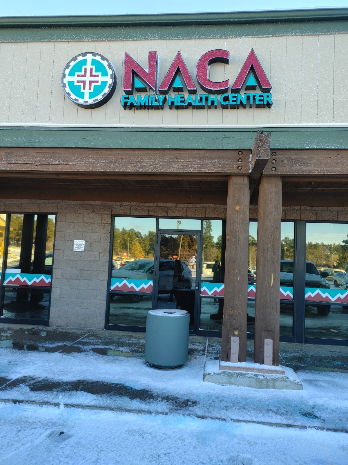 Exterior photograph showing NACA Family Health Center entrance, parking lot, and facility signage with clear skies
