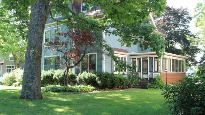 Exterior view of two-story residential facility with blue siding, mature trees, and manicured lawn.