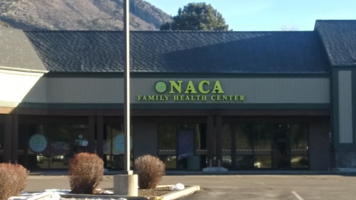 Exterior view of NACA Family Health Center with mountain backdrop, parking area, and building entrance