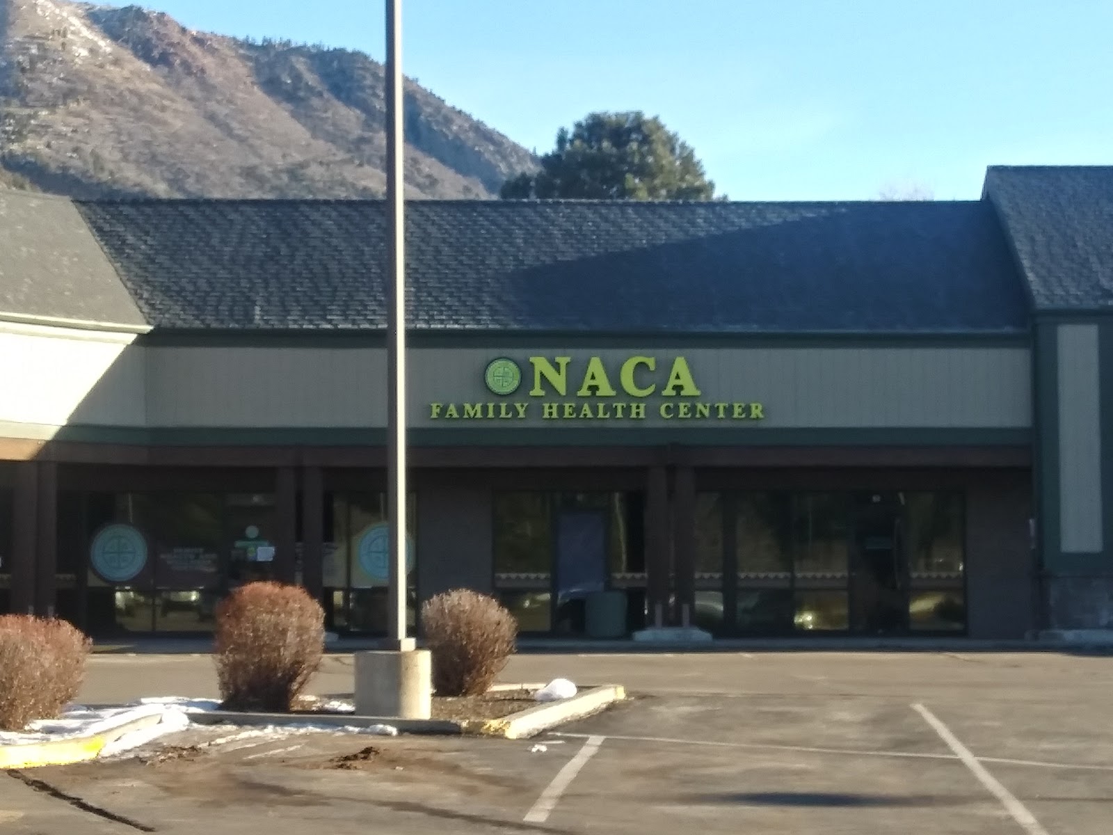 Exterior view of NACA Family Health Center with mountain backdrop, parking area, and building entrance