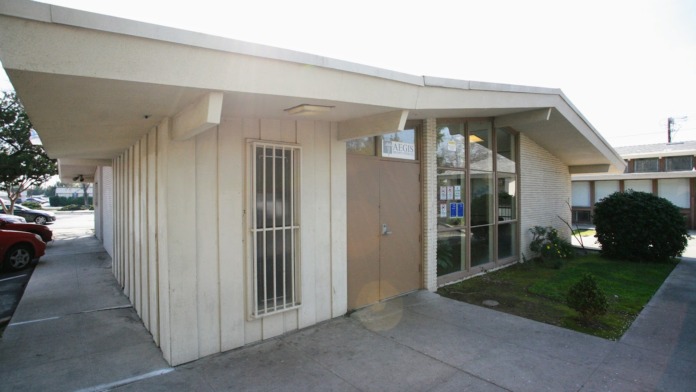 Exterior view of facility showing main entrance, covered walkway, parking area, and green landscape