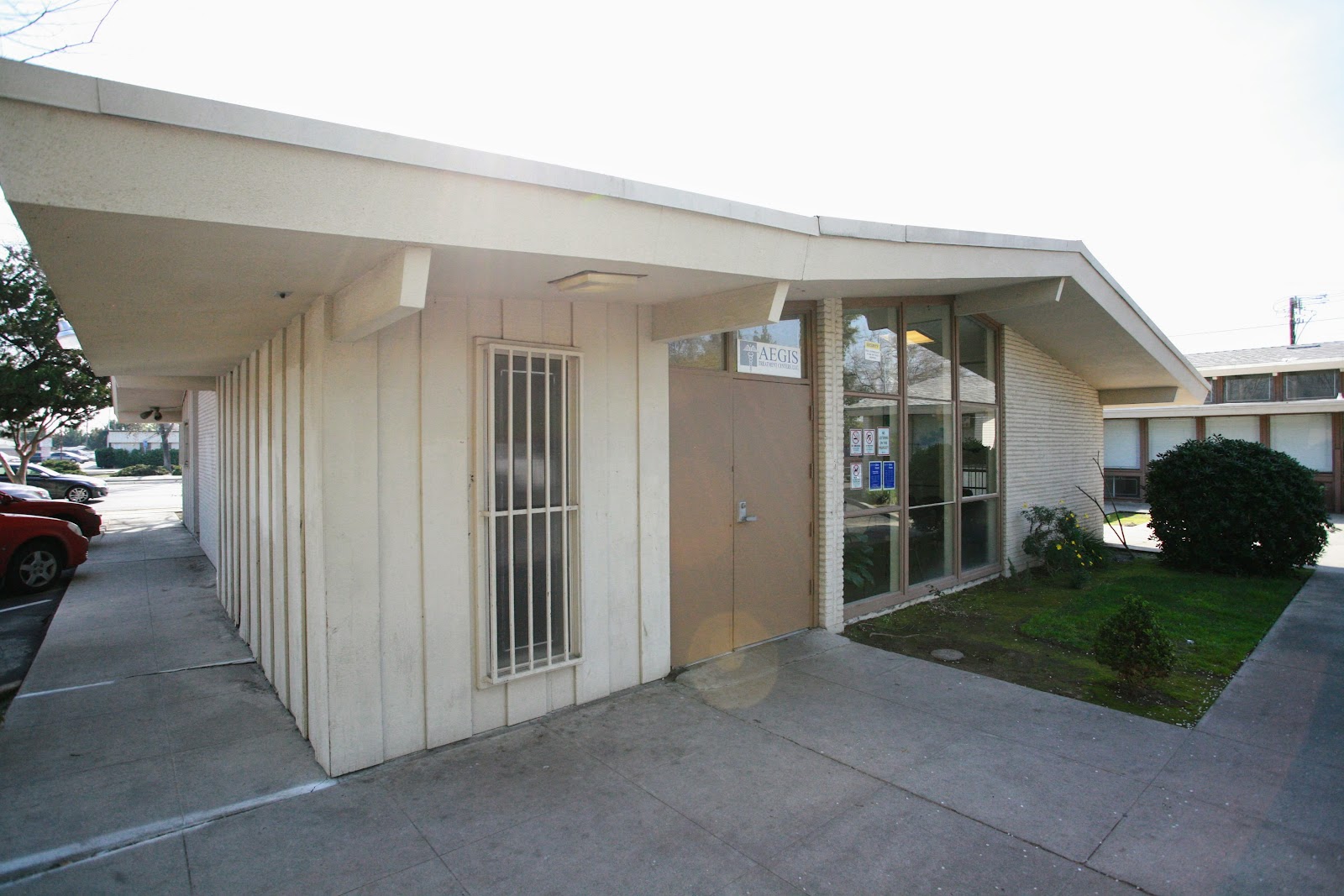 Exterior view of facility showing main entrance, covered walkway, parking area, and green landscape