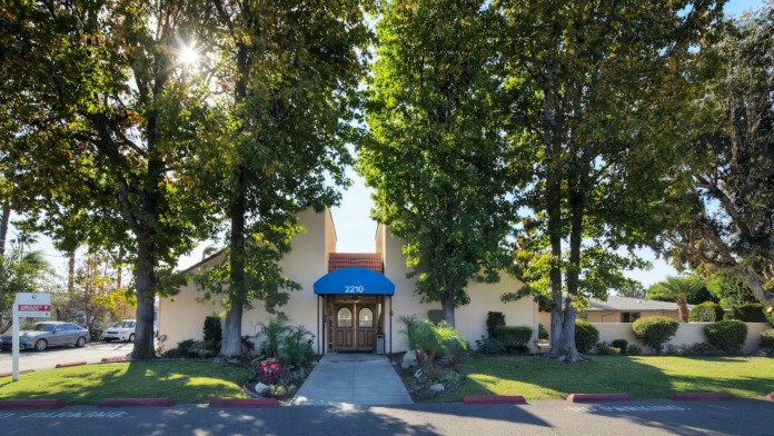 Exterior front view showing facility building facade with manicured lawn, flowering landscaping and large mature trees