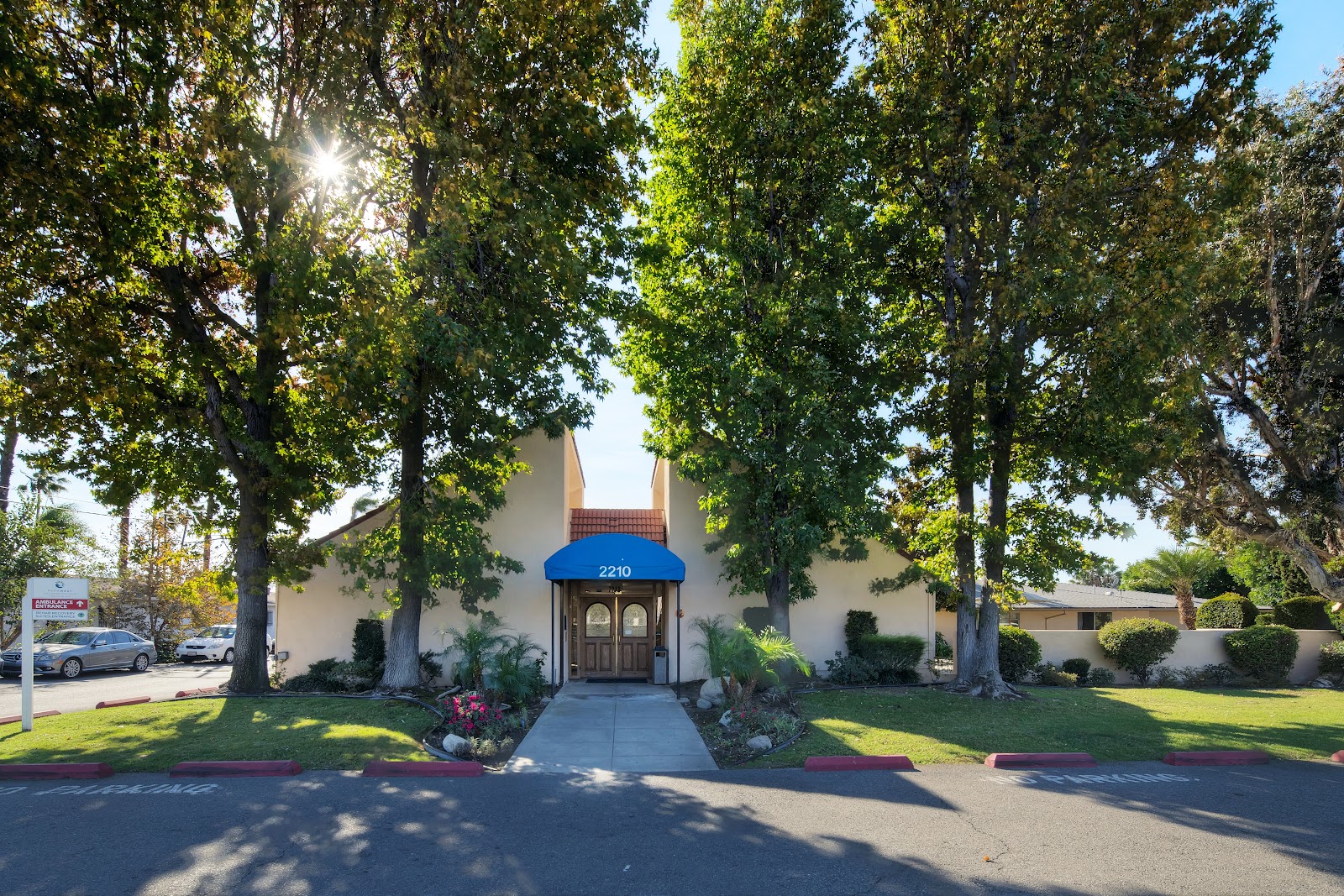 Exterior front view showing facility building facade with manicured lawn, flowering landscaping and large mature trees