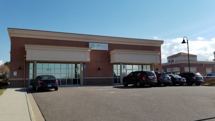 Exterior front showing dual glass entrance doors, brick facade, accessible parking spaces, and vehicles