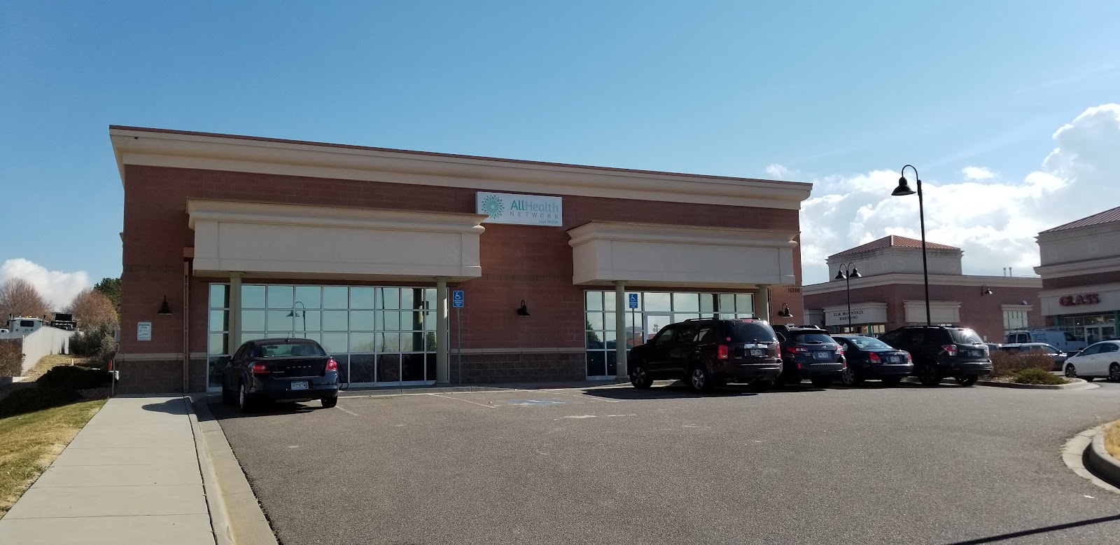 Exterior front showing dual glass entrance doors, brick facade, accessible parking spaces, and vehicles