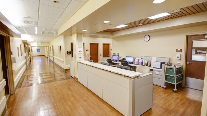Interior reception area with white desk, computer workstations, medical equipment, hallway with handrails and warm lighting