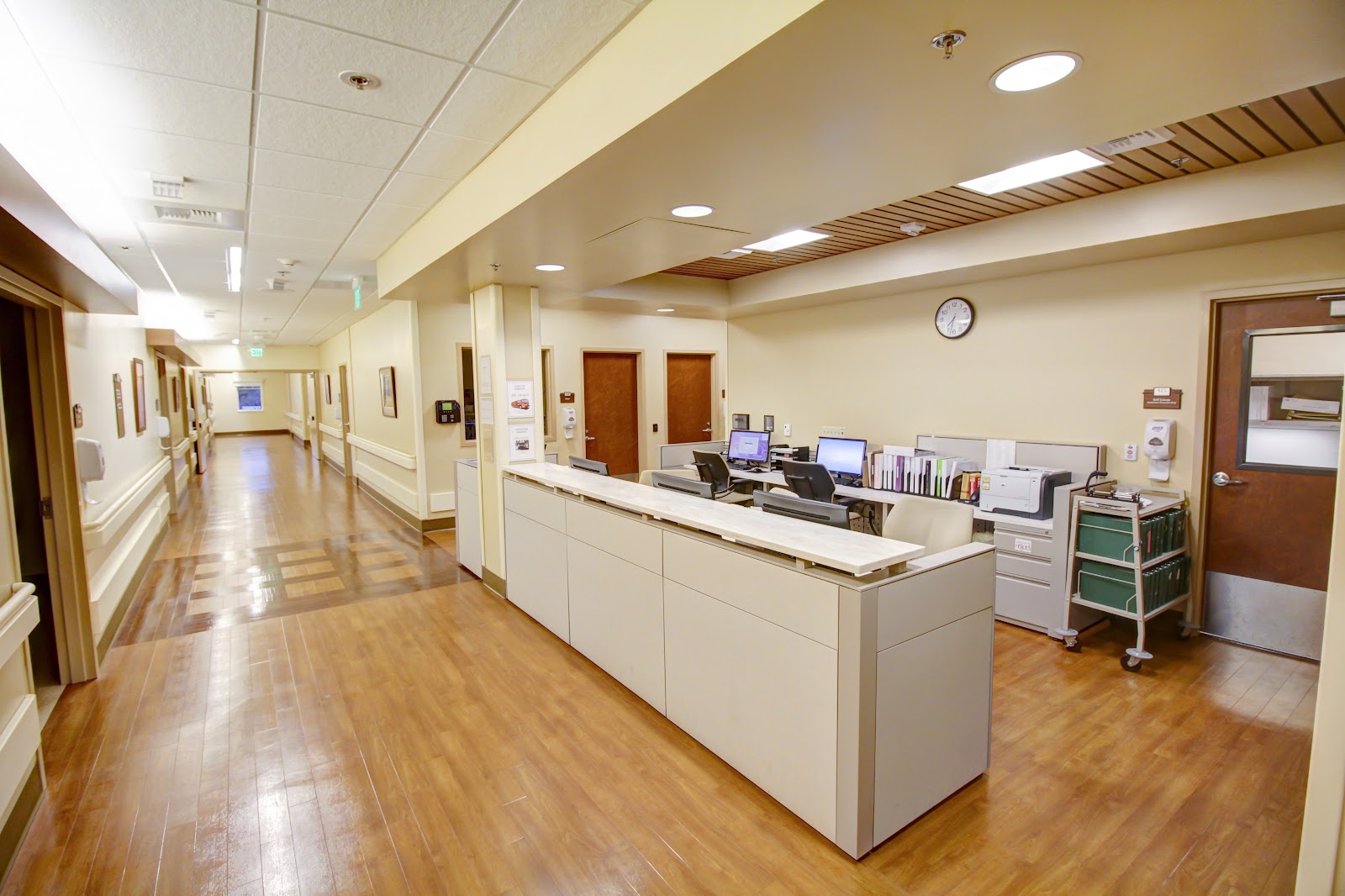 Interior reception area with white desk, computer workstations, medical equipment, hallway with handrails and warm lighting