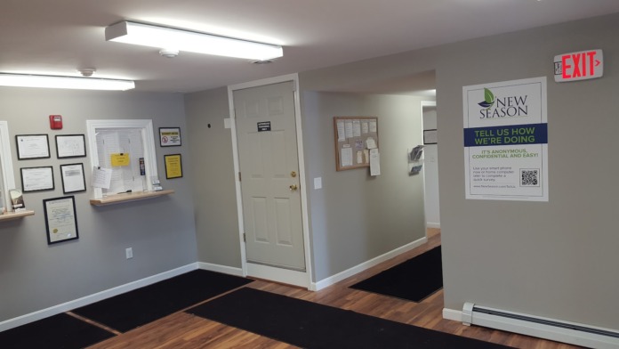 Interior reception area with framed certifications on walls, service counter, EXIT sign, and New Season branding signage