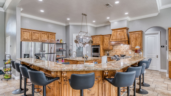 Interior kitchen space with wooden cabinetry, granite counters, island seating, and stainless steel appliances