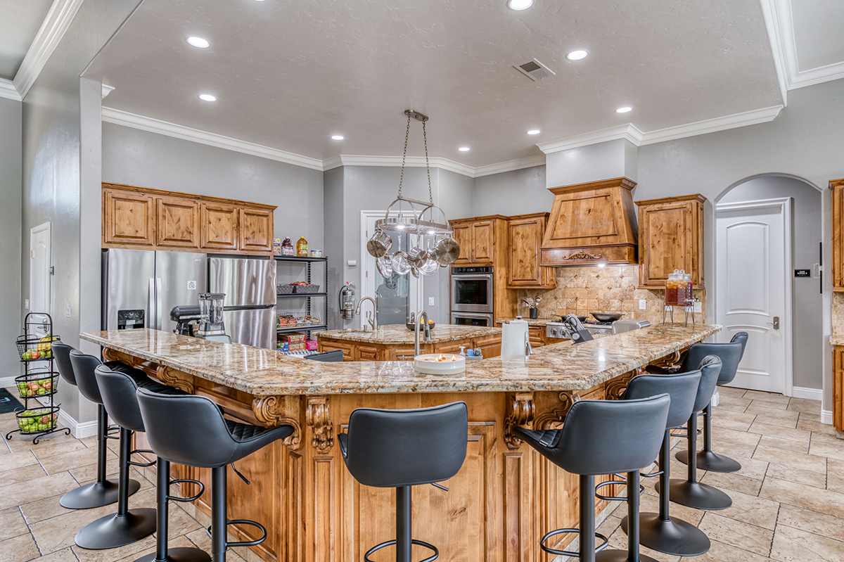 Interior kitchen space with wooden cabinetry, granite counters, island seating, and stainless steel appliances
