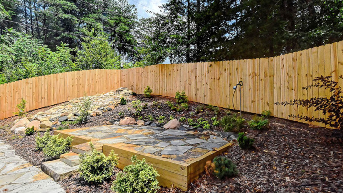 Outdoor garden area with stone patio, wooden raised planter beds, landscaping, and wooden fence