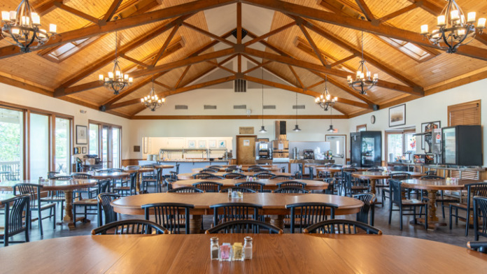 Interior dining hall with exposed wood beam vaulted ceiling, multiple tables, chairs, and large windows