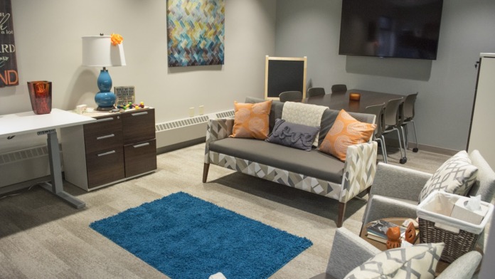Interior room with gray sofa, orange pillows, blue area rug, wall-mounted television, and artwork.