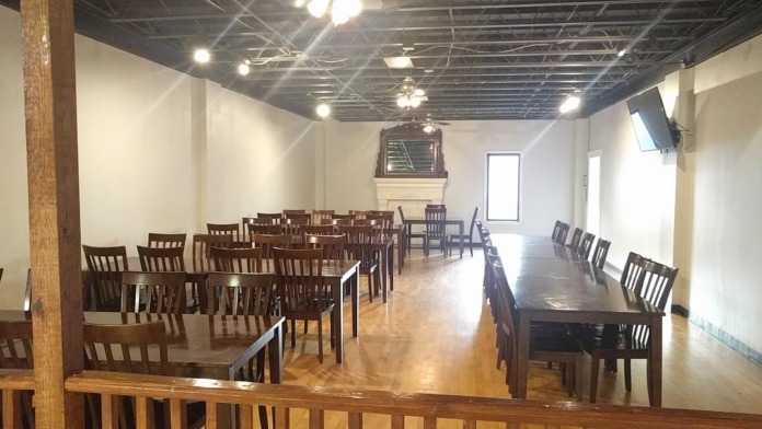 Interior dining area with multiple wooden tables, chairs, and exposed beam ceiling with bright lighting
