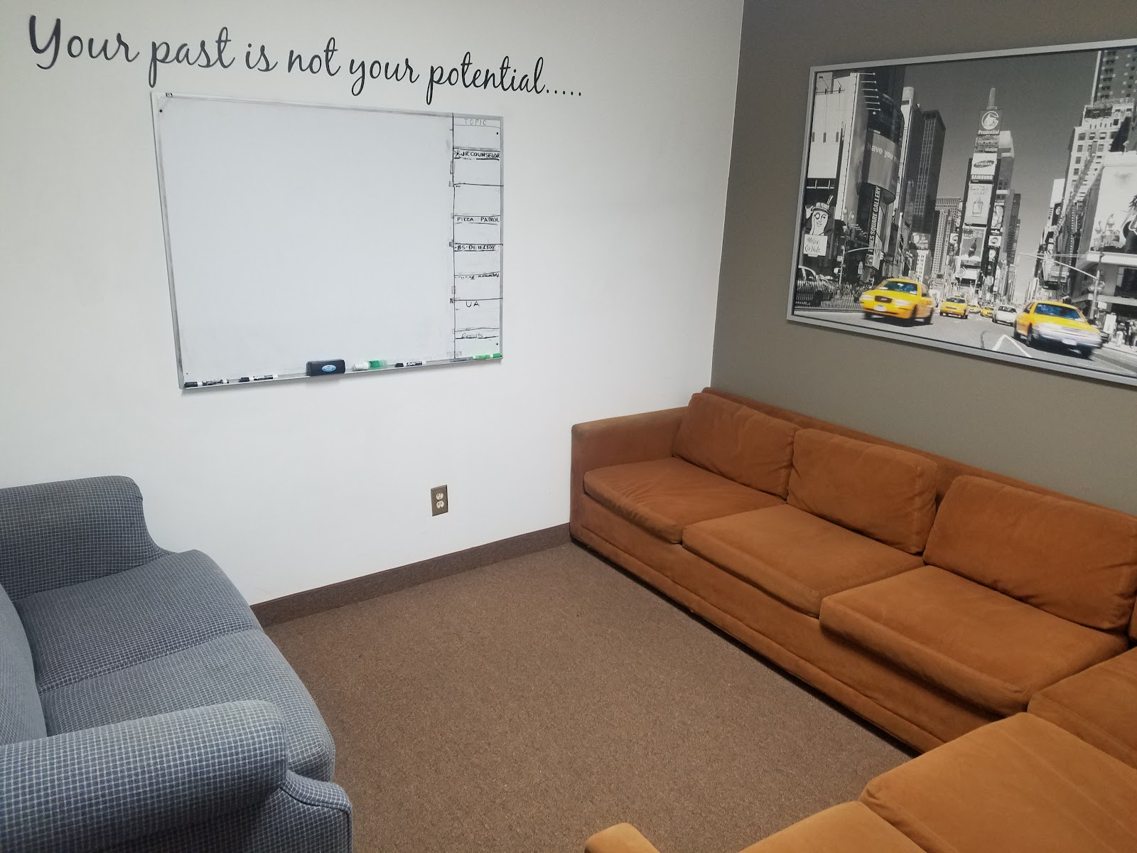 Interior meeting space with upholstered seating, whiteboard, and motivational wall messaging