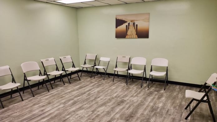 Interior meeting room with arranged folding chairs in semicircle, landscape wall art, drop ceiling lighting, and neutral walls