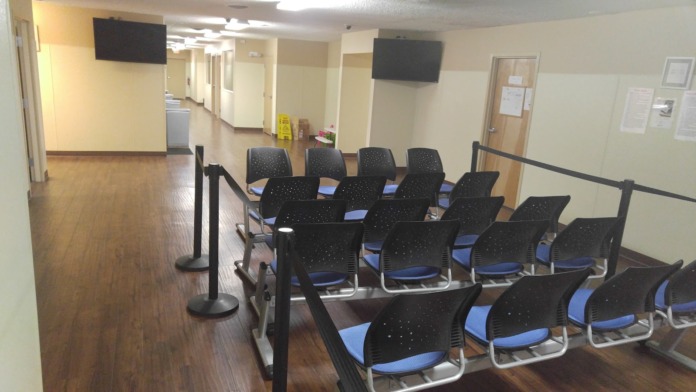 Interior group space with rows of black and blue chairs, monitor display, wooden flooring