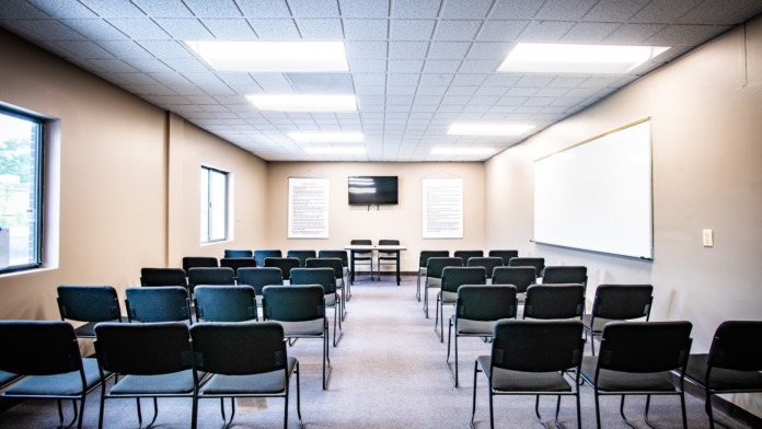 Interior group meeting room with rows of black and blue chairs arranged theater-style, ceiling lights, and informational wall posters
