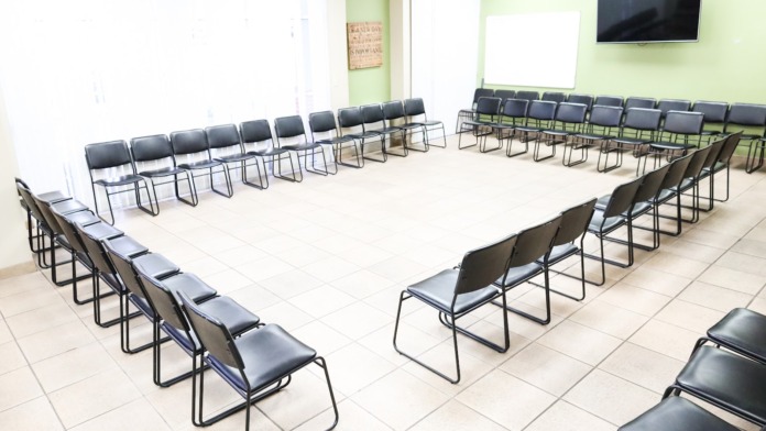 Interior group session room with rows of chairs arranged in circle configuration, green walls, and television