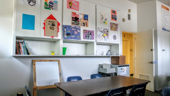 Interior activity room with table, black chairs, turquoise accent wall, informational posters, and plant