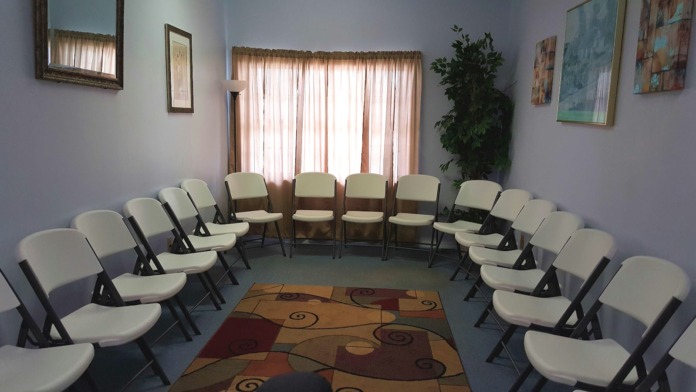 Interior therapy room with multiple cream-colored padded chairs arranged in circle formation, windows with natural light