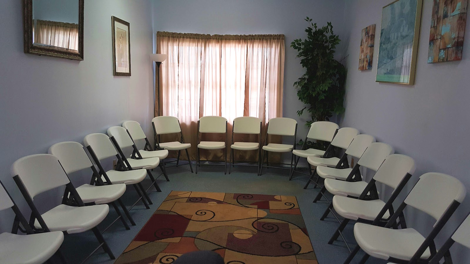 Interior therapy room with multiple cream-colored padded chairs arranged in circle formation, windows with natural light