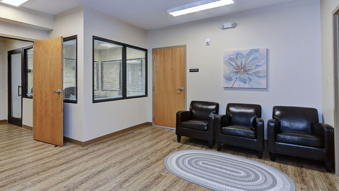 Interior therapy space with three black leather chairs, oval floor mat, blue flower artwork, and glass observation windows