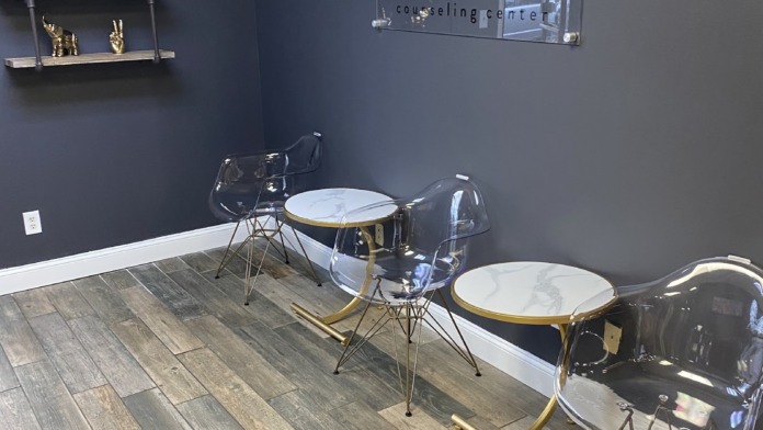 Interior therapy space with dark blue walls, modern seating with gold accents, facility logo, decorative shelving, and wood flooring